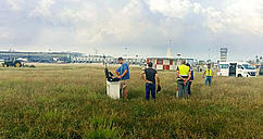 Engineers and field personnel preparing drone-based RF measurements in a grassy field near a Mexican airport for SENEAM